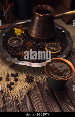 Eine Tasse Kaffee auf dem Hintergrund eines Vintage-Silbertablett mit Kaffeebohnen, Gewürzen und Blumen auf einem Tisch aus alten strukturierten Holzbrettern Stockfoto