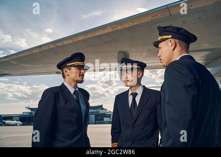 Drei kaukasische Piloten, die neben einem Flugzeugflügel stehen Stockfoto