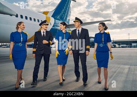 Lächelnde Stewardessen und Flugbegleiter, die am Flugplatz entlang gehen Stockfoto