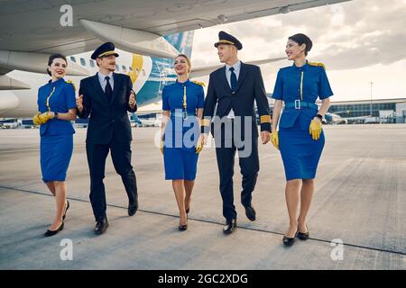 Wunderschöne Stewardessen und hübsche Flieger, die auf dem Flugplatz spazieren Stockfoto