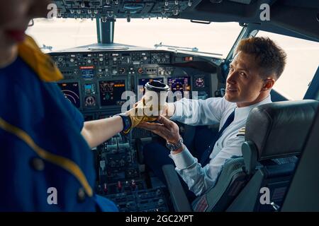 Stewardess, die einem erfreuten Co-Piloten im Cockpit Kaffee serviert Stockfoto