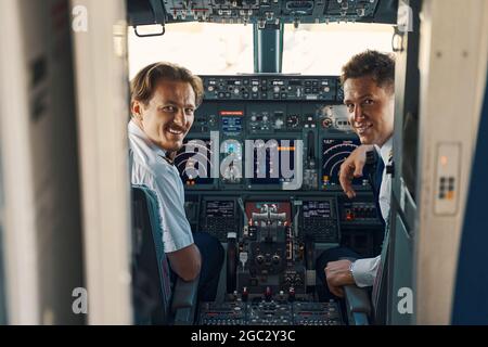 Fröhlicher Pilot und ein Co-Pilot, der aus dem Cockpit schaut Stockfoto