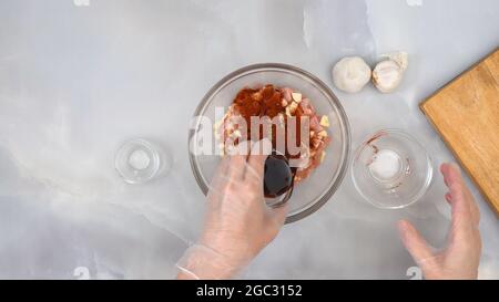 Gehacktes Hühnerfilet, mariniert mit Knoblauch, Gewürzen, Paprika und Sojasauce, in einer Glasschüssel auf Marmorboden Stockfoto