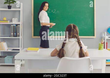 Schulkind sitzt am Schreibtisch und hört aufmerksam dem Lehrer im modernen Klassenzimmer zu Stockfoto