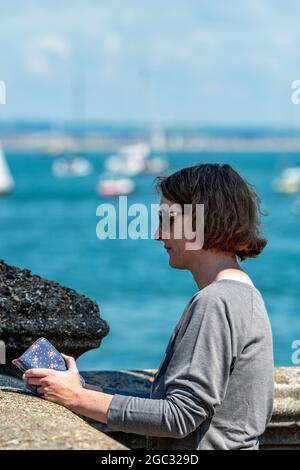 Frau per Smartphone, Frau per Telefon, Frau am Meer per Telefon, Frau im Urlaub, Nachrichten checken, Frau an der Küste mit Telefon, Urlaub Stockfoto