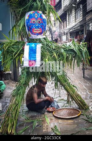 Kathmandu, Bagmati, Nepal. August 2021. Ein Mann, der sich als Dämon verkleidet, sitzt während des Ghantakarna-Festivals in Kathmandu, Nepal, am 6. August 2021 unter dem Bildnis eines Dämons. Die Gemeinde Newar im Kathmandu Valley beobachtet Ghantakarna, ein Fest, das böse Geister vertreiben und Glück einläuten soll. Die Menschen tragen Metallringe, um sich vor allem Übel und bösen Geistern zu schützen. (Bild: © Sunil Sharma/ZUMA Press Wire) Stockfoto