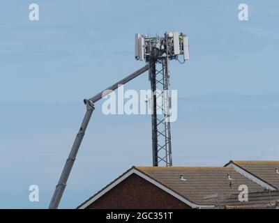 Eine große Kirsche Picker Stil Power-Plattform ruht auf einem Handy-Mast.Arbeiter in orange Harthüte machen Reparaturen an der Telekommunikation.angesehen Stockfoto