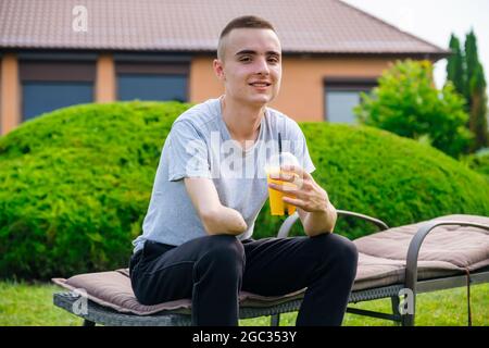 Ein Mann mit einem amputierten Arm sitzt auf einer Sonnenliege und trinkt einen Cocktail im Garten Stockfoto