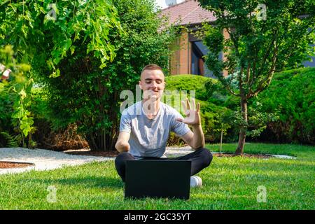 Kerl mit amputierten Arm sitzt auf dem Rasen und im Gespräch mit Freunden über soziales Netzwerk Stockfoto