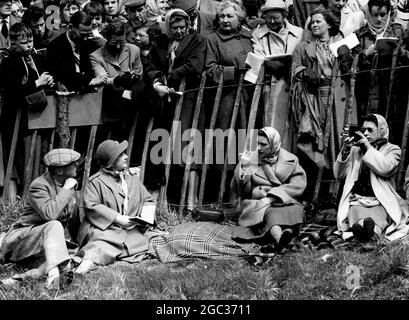 The Crowd Sehen Sie sich die Dreharbeiten der Queen an nur ein enger Zaun trennt die Menge von Mitgliedern der königlichen Familie, die am zweiten Tag der drei-Tage-Pferdetrials in Badminton, Gloucestershire, teilnehmen. Der Herzog von Beaufort, Gastgeber der königlichen Besucher, und die Königin-Mutter beobachten, wie die Königin die Teilnehmer beim Steinbruch-Sprung auf dem Langlaufkurs filmt. Prinzessin Margaret, die wie ihre Schwester einen Kopftuch gegen den kalten Wind trägt, raucht eine Zigarette. April 1957 Stockfoto