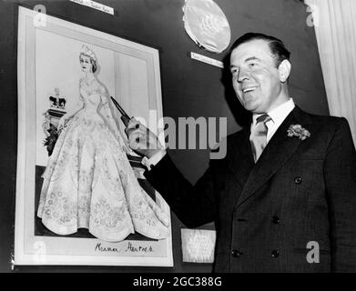 Norman Hartnell sah mit seiner Skizze des Kleides der Königin, das für die Krönung getragen werden soll, das in weißem Satin mit dem Emblem von Großbritannien und dem Commonwealth bestickt ist. Juni 1953 Stockfoto