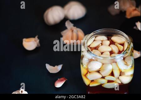 Fermentierte Knoblauchzehen in einem Glas Honig, eine reiche Quelle von Probiotika, über einem rustikalen Holzhintergrundtisch. Selektiver Fokus mit unscharfem Hintergrund Stockfoto