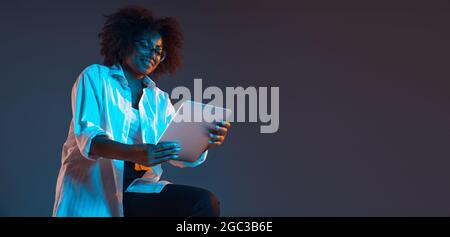 Portrait von afrikanischen jungen Mädchen in weißem Hemd mit Tablet, Gadget isoliert auf dunkelblauen Studio-Hintergrund. Konzept der menschlichen Emotionen, Gesichts Stockfoto