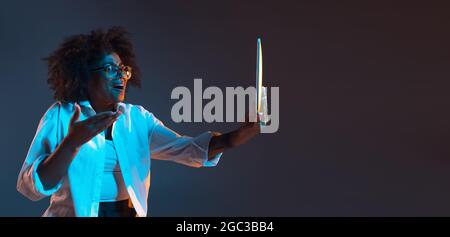 Portrait von afrikanischen jungen Mädchen in weißem Hemd mit Tablet, Gadget isoliert auf dunkelblauen Studio-Hintergrund. Konzept der menschlichen Emotionen, Gesichts Stockfoto