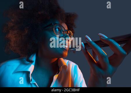 Portrait von afrikanischen jungen Mädchen in weißem Hemd mit Telefon, Gadget isoliert auf dunkelblauen Studio-Hintergrund. Konzept der menschlichen Emotionen, Gesichts Stockfoto