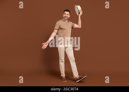 Foto von aufgeregt ziemlich junge Kerl gekleidet beige Kleidung lächelnd halten Kopfbedeckung isoliert braune Farbe Hintergrund Stockfoto
