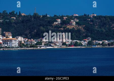 Blick auf Zakynthos, die Hauptstadt der griechischen Insel, mit flachen Gebäuden am Wasser. Landschaft der orthodoxen Kirche um rote Ziegelhäuser neben ruhigen Meer & Hügel. Stockfoto