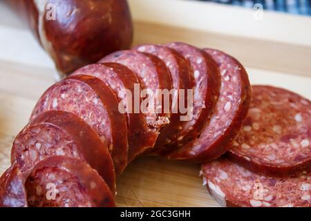 Geschnittene türkische Wurst (türkisch: Sucuk) auf einem Schneidebrett. Eine getrocknete würzige Wurst auf Holzhintergrund. Stockfoto