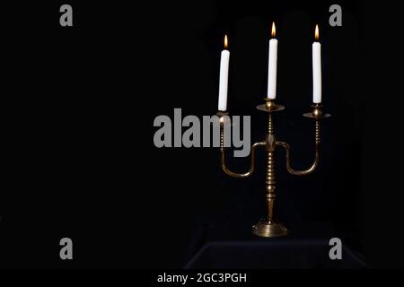 Antiker Kupferkandelständer mit drei brennenden weißen Kerzen auf schwarzem Hintergrund isoliert, Kopierraum, Nahaufnahme. Kann als Designelement verwendet werden Stockfoto