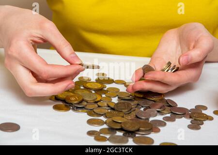 Geld sparen, eine Hand legt Münzen in eine andere Hand, auf einem hellen Tisch sind Münzen aus verschiedenen Ländern, Nahaufnahme. Stockfoto