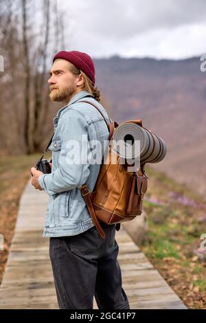 Junger Mann mit braunem Rucksack, der im Frühling die Natur erkundet und alleine im Freien unterwegs ist. Wanderer im lässigen Outfit Reisen in Wäldern. Landschaften auf dem Land, Stockfoto