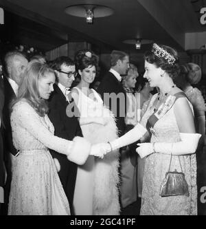 Queen Elizabeth II schüttelt sich die Hände mit Ursula Andress im Odeon Theatre, Leicester Square, London für die Royal Film Performance 1966, wo sie den Film Born Free in Aid of the Cinema and Television Benevolent Fund sehen soll. In der Linie ist Woody Allen und Raquel Welch . 14. März 1966 Stockfoto