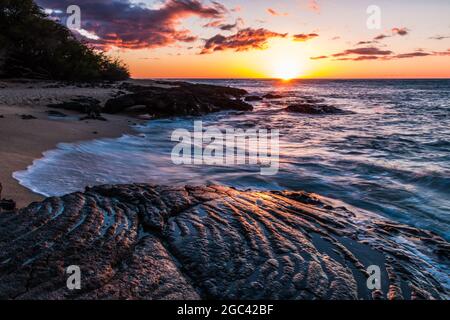 Wellen, die über den uralten Lavastrom am Kapalaoa Beach bei Sonnenuntergang, Anaeho'omalu Bay, Hawaii Island, Hawaii, USA, waschen Stockfoto