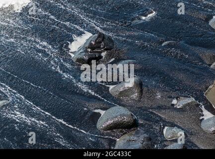 Nahaufnahme der Wellen Waschen über Felsbrocken und schwarzem Sand am Kaimu Black Sand Beach, Hawaii Island, Hawaii, USA Stockfoto