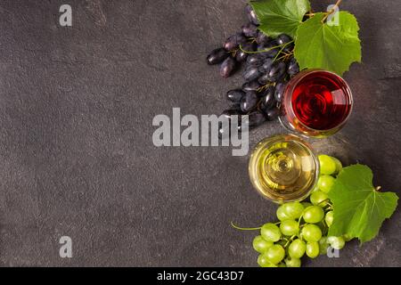 Gläser mit Rot- und Weißwein und Traubenvielfalt auf schwarzem Tisch von oben. Weinkomposition mit Kopierraum für Design. Stockfoto