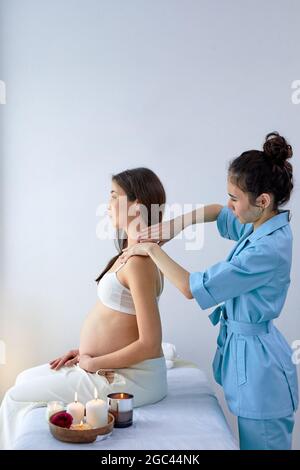 Schöne gravid asiatische Brünette Frau genießen Rücken und Schultern Massage in Kosmetikerin Zimmer im Spa-Center, Seitenansicht auf entspannte Dame auf dem Bett sitzen, Stockfoto