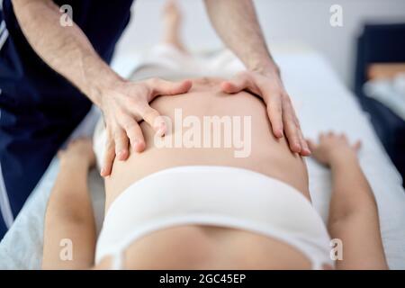 Schwanger junge Frau mit schöner Haut auf dem Bett liegend mit entspannende pränatale Massage, Physiotherapeutin tut verschiedene Techniken für eine bessere Massage, Stockfoto