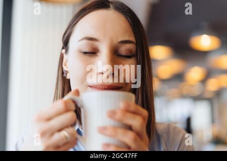 Attraktive Frau mit niedlichem Lächeln mit einem Kaffee beim Entspannen In Pause Stockfoto