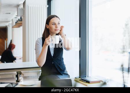 Attraktive Frau mit niedlichem Lächeln mit einem Kaffee beim Entspannen In Pause Stockfoto
