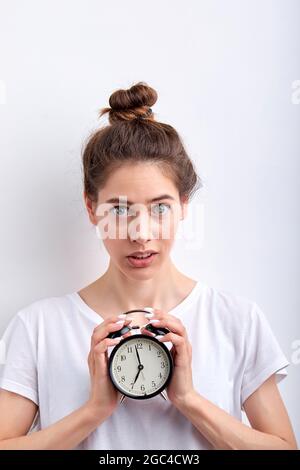 Foto-Porträt der jungen Frau halten Wecker spät für Frist betont isoliert auf weißem Hintergrund. Kaukasische Dame in lässiger T-Shirt-Optik Stockfoto