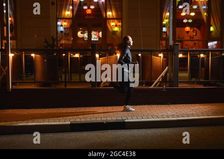 Läufer, Fitness und sportliche Motivation. Starke athletische Frau läuft in der Nacht Stadt mit gelben Lichtern Girlanden.Kaukasische weibliche Modell trägt b Stockfoto