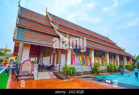 LAMHPUN, THAILAND - 8. MAI 2019: Historisches Gebäude von Viharn Luang mit Giegeldach, Säulen, bedeckt mit Reliefmustern und farbenfroher Lanna f Stockfoto