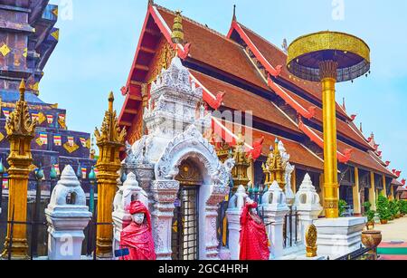 Das Pyathat (Giebel) Dach des Viharn Luang ist hinter dem vergoldeten chatra zeremoniellen Regenschirm und Stucktor des Chedi von Wat Phra That Lampang zu sehen Stockfoto