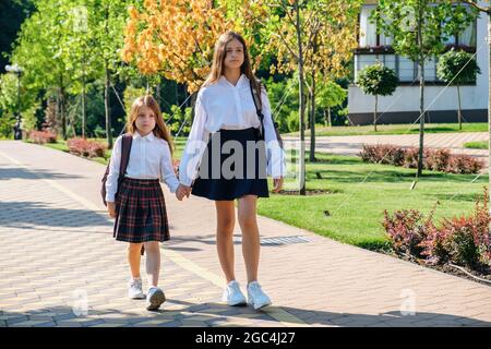 Zwei Schwestern halten sich die Hände und gehen am Morgen gemeinsam zur Schule Stockfoto