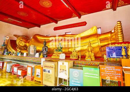 LAMHPUN, THAILAND - 8. MAI 2019: Innenraum des Bilderhauses mit großem goldenen, rückenden Buddha und kleinen Bildern von Buddha davor, Wat Phra Tha Stockfoto
