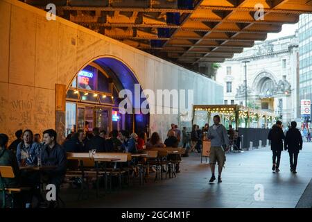 London, Großbritannien, 6. August 2021: Am Freitagabend auf der Londoner South Bank haben Trinker Zeit für ein Pint und ein wenig Geselligkeit am Waterloo Tap, wobei die Waterloo Station im Hintergrund bereit ist, Trinker sicher mit öffentlichen Verkehrsmitteln nach Hause zu bringen. Obwohl die Besucherfrequenz nicht so hoch ist wie in Zeiten vor der Pandemie, herrscht immer noch eine gute Stimmung am Freitagabend, da sich die Menschen auf das Wochenende freuen. Anna Watson/Alamy Live News Stockfoto