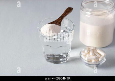 Kollagenpulver im Löffel auf Glas Wasser, Kollagenkapseln und Glas Pulver auf hellblauem Hintergrund. Speicherplatz kopieren Stockfoto