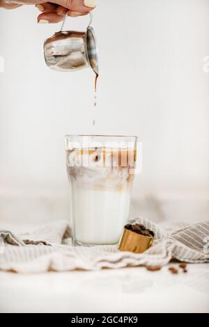 Weibliche Hand gießt frischen Espresso und macht Iced Latte Kaffee Stockfoto