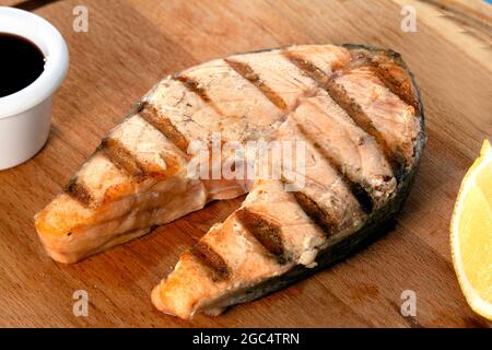 Frisch zubereitetes, köstliches Lachssteak mit Gewürzen und Kräutern, gegrillt. Gesunde Meeresfrüchte mit Sauce und Zitrone auf Holzplatte Stockfoto