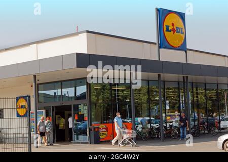 Menschen vor dem berühmten Budget-Lebensmittelgeschäft Lidl einkaufen für Lebensmittel und andere Waren mit ihren Trolleys verlassen. Jeder trägt Gesichtsmasken. Stockfoto