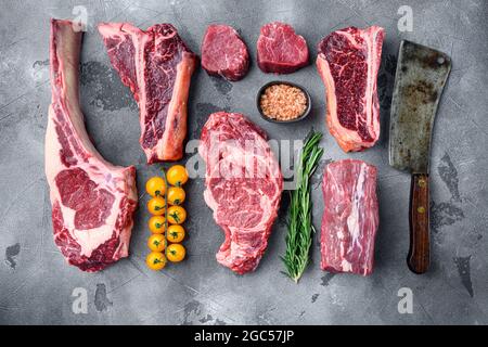 Rohe Rindersteaks, Tomahawk, T-Bone, Clubsteak, Rib-Eye- und Filet-Schnitte, auf grauem Steingrund, Draufsicht flach liegend Stockfoto