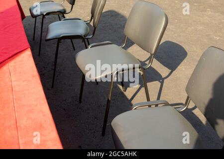Schwarze Stühle auf der Straße. Sitze in der Nähe des roten Tisches. Gartenmöbel. Plätze für Teilnehmer. Stockfoto