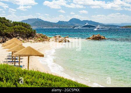 (Selektiver Fokus) atemberaubender Blick auf den Strand von Capriccioli, der an einem sonnigen und windigen Tag von einem türkisfarbenen und rauhen Wasser umspült wird. Stockfoto