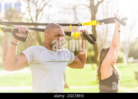 Fitness-Paar macht Arme und Bizeps trainieren mit Fitness-Gurte im Park Stockfoto