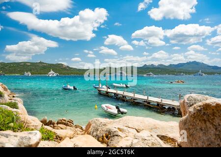 (Selektiver Fokus) atemberaubender Blick auf den Strand von Capriccioli, der an einem sonnigen und windigen Tag von einem türkisfarbenen und rauhen Wasser umspült wird. Stockfoto