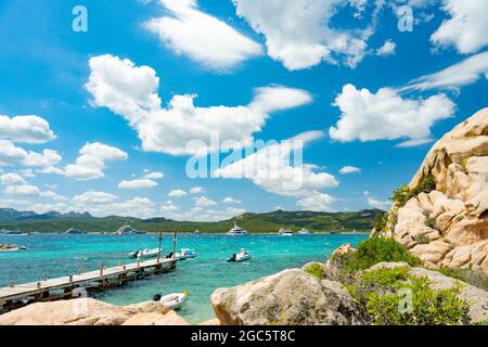 (Selektiver Fokus) atemberaubender Blick auf den Strand von Capriccioli, der an einem sonnigen und windigen Tag von einem türkisfarbenen und rauhen Wasser umspült wird. Stockfoto